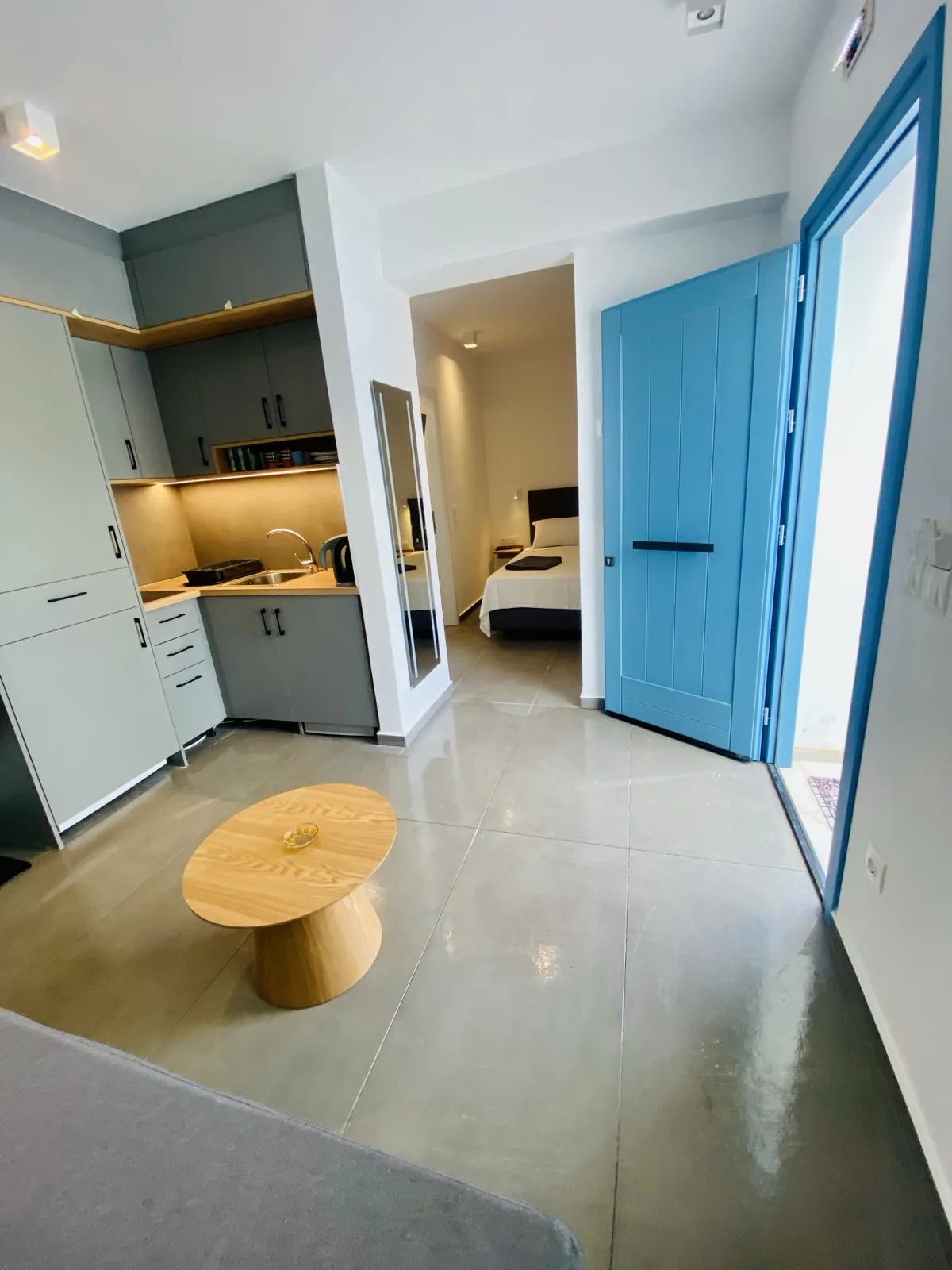 Open-plan quad room with kitchenette, dining area and bedroom beyond the blue entrance door